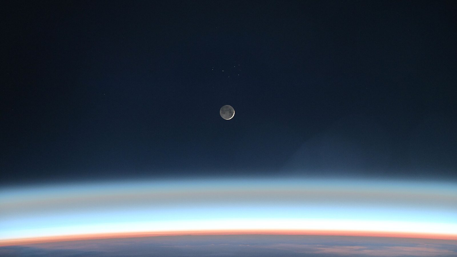 Lua crescente vista da Estação Espacial Internacional, acima da faixa colorida da atmosfera da Terra