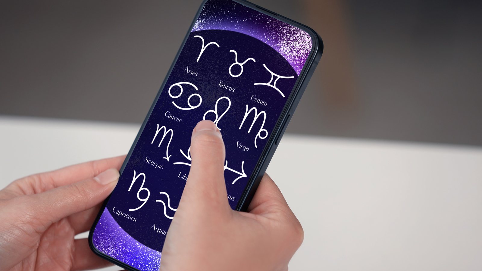 Mãos seguram um celular com a tela de um aplicativo de astrologia mostrando os símbolos dos doze signos