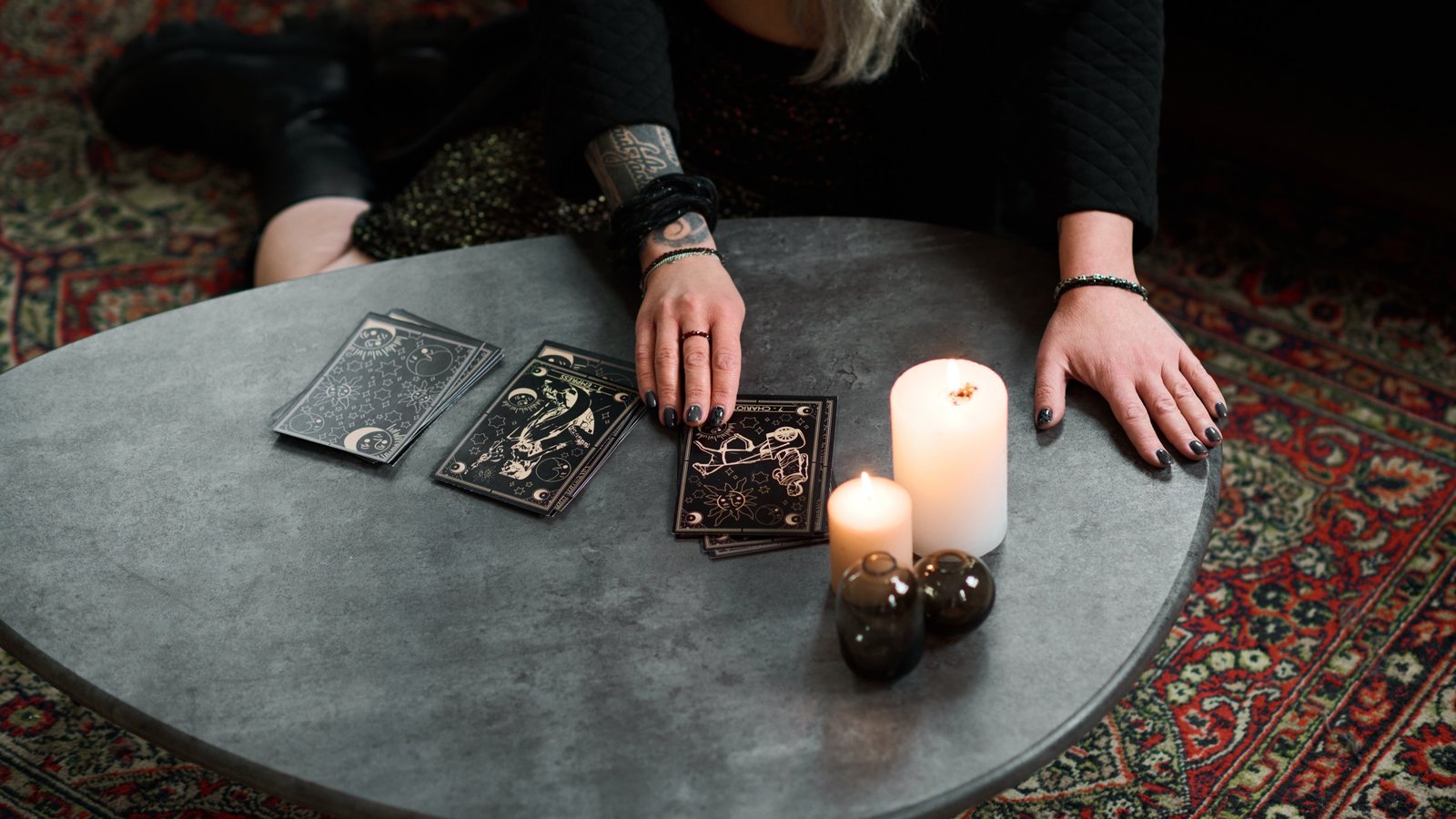 Três cartas de tarô abertas sobre toalha azul, com o baralho em leque e velas ao fundo